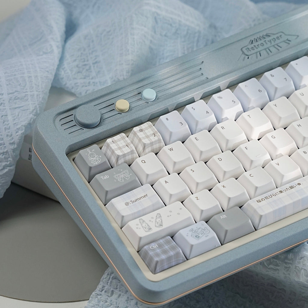 A retro-style mechanical keyboard with a dusty blue-gray frame and white, light gray, and plaid keycaps, styled on a light blue textured fabric surface.