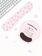 A pink ergonomic wrist rest and matching keyboard pad set with cute baking-themed illustrations, shown on a white polka-dotted desk surface next to a keyboard.