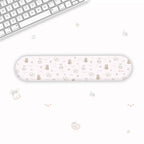 A long, narrow wrist rest with a cute pastel cartoon pattern of bears, hearts, and flowers, displayed on a clean white desk next to a keyboard.