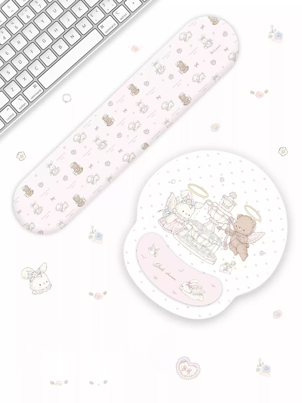 A pastel pink computer mouse pad and matching wrist rest set with cute cartoon angel and teddy bear illustrations, styled on a white desk next to a keyboard.