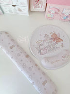A pastel pink and white desk accessory set featuring a cartoon mouse pad with angel and cake illustrations, a matching cylindrical wrist rest, and a small pink storage organizer in the background.