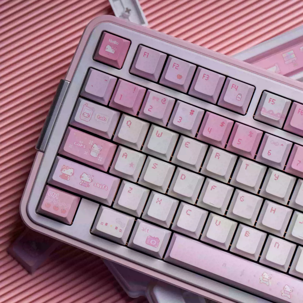 A close-up of a compact mechanical keyboard with pastel pink and white keys, decorated with cute Hello Kitty illustrations, resting on a pink ribbed surface.