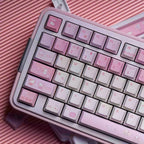 A close-up of a compact mechanical keyboard with pastel pink and white keys, decorated with cute Hello Kitty illustrations, resting on a pink ribbed surface.