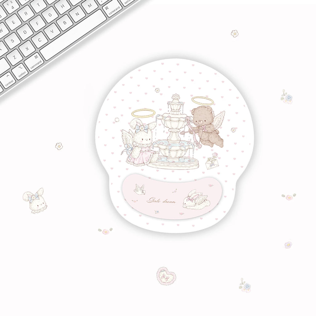 A round gel mouse pad with a pastel illustration of a fountain and two angel characters, shown on a white desk next to a keyboard. The pad has a pink wrist rest and the text 'Sweet dream' on it.